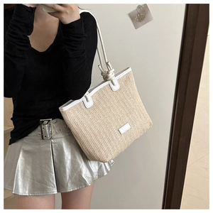 Detail of woven straw tote bag featuring white leather trim and knotted rope handle