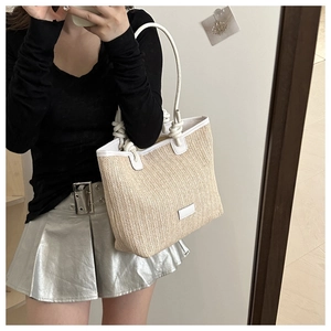 Detail of woven straw tote bag featuring white rope handle and faux leather trim design