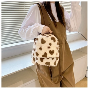 Detail of plush cow print backpack with heart patterns and adjustable straps on a model