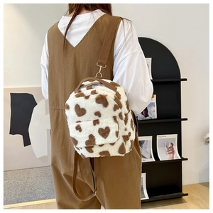 Detail of plush cow print backpack with heart patterns and adjustable straps on a model