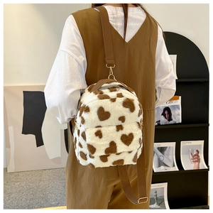 Detail shot of plush cow-print backpack featuring brown heart pattern and golden zipper