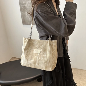 Chic beige tote bag with bamboo leaf pattern and metal chain strap on female model