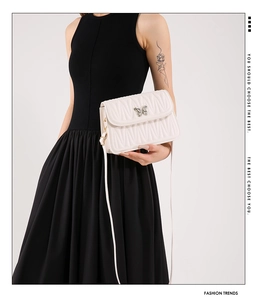 Detail view of white quilted crossbody bag with wavy flap and silver butterfly buckle