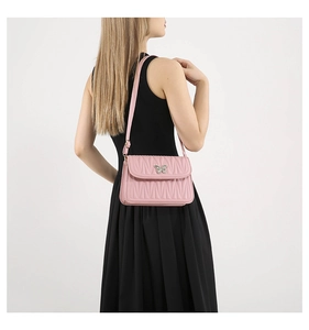 Detail of pink quilted shoulder bag featuring metal butterfly buckle on black dress