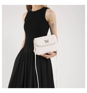 Close-up of white quilted shoulder bag with elegant butterfly metal clasp on black dress