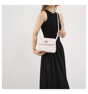 Close-up of white quilted crossbody bag with a silver butterfly buckle on a black dress