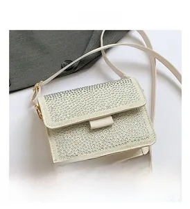 Detailed close-up of a white leather crossbody bag featuring sparkling silver rhinestones