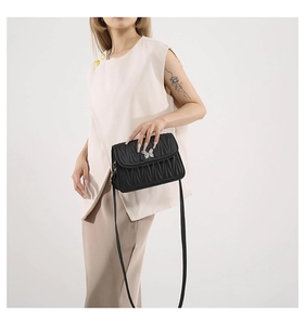 Detail of black quilted shoulder bag featuring silver butterfly clasp and leather strap