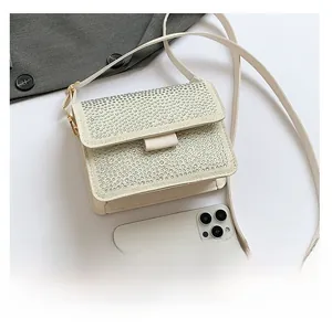 Detail view of mini white rhinestone shoulder bag shown with smartphone for scale
