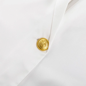 Detailaufnahme eines weißen Blazers mit geprägtem goldenem Wappenknopf und strukturierter Textur