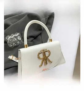 Detail of white leather crossbody bag with bold golden R-shaped metal buckle and strap