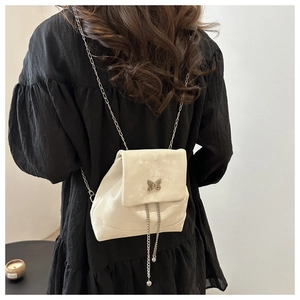 Detail of a creamy leather backpack featuring a metal bow and silver chain tassels