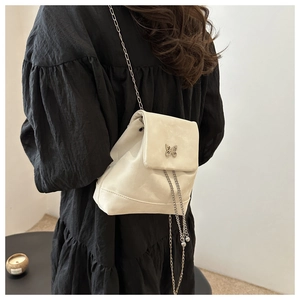 Detail of cream PU leather backpack featuring metal butterfly and silver chain strap