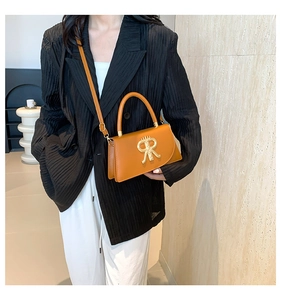 Caramel leather crossbody bag with gold metal logo worn by a model in a stylish outfit