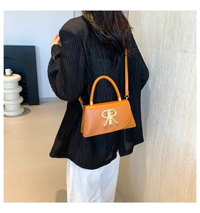 Orange-brown leather handbag with R-shaped gold metal logo worn by a model