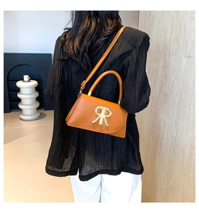 Rear view of model wearing a brown leather crossbody bag with golden R-shaped metal logo