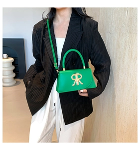 Detail of bright green structured crossbody bag with gold R logo on black blazer