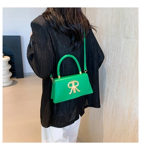 Green leather crossbody bag featuring a large gold R-letter metal buckle on a black coat
