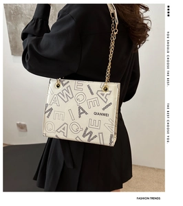 Detail of cream leather tote bag featuring black letter prints and gold chain strap