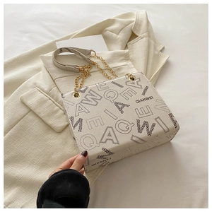 Detailed view of cream tote bag featuring black letter prints and gold chain strap