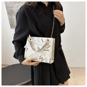 Detailed view of white tote bag with black letter patterns and gold metal chain strap