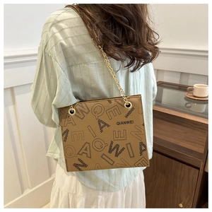 Detail of vintage brown tote bag with letter print and gold chain strap on shoulder