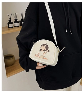 Close-up of cream canvas crescent crossbody bag with minimalist cartoon girl illustration