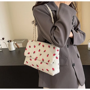 Detail showing white corduroy shoulder bag with red strawberry embroidery and chain strap