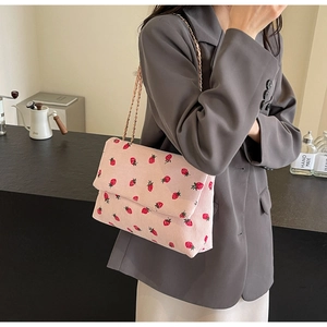 Detail of pink corduroy shoulder bag with red strawberry print and golden chain strap