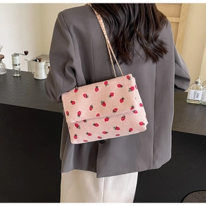 Close-up of pink corduroy shoulder bag with strawberry prints and metal chain strap