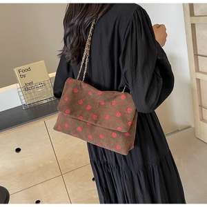 Detail of dark brown corduroy shoulder bag with red strawberry embroidery and chain