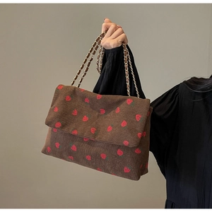 Detail of dark brown corduroy tote bag with red strawberry embroidery and chain strap