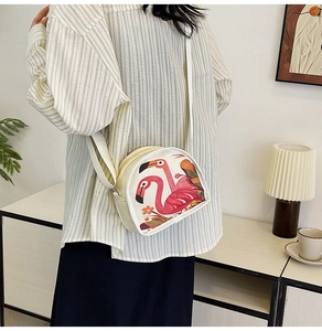 Detail of canvas crescent crossbody bag with flamingo print worn by a model in casual setting