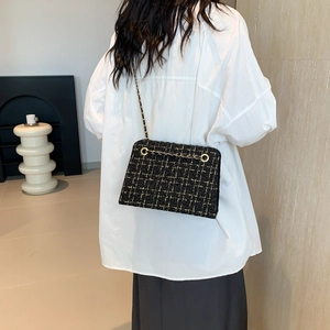 Elegant black and gold tweed chain shoulder bag worn by model in a modern interior