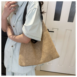 Macro detail of khaki straw woven tote bag with black fabric straps on a light blue shirt
