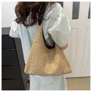 Detail of hollow woven shoulder bag in beige with black trim on a female model