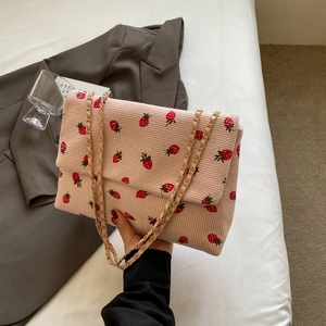 Pink corduroy strawberry tote bag with gold chain strap shown in a lifestyle setting