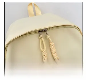 Detailed close-up of smooth double zipper with woven puller on cream nylon backpack