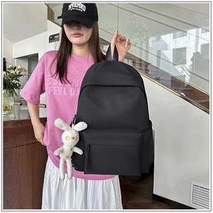 Detail of black minimalist backpack featuring a plush white bunny charm on the side pocket