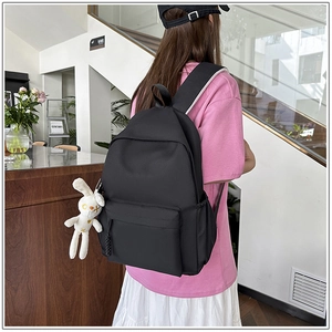Detail view of black nylon backpack with a white rabbit plush charm and side pockets