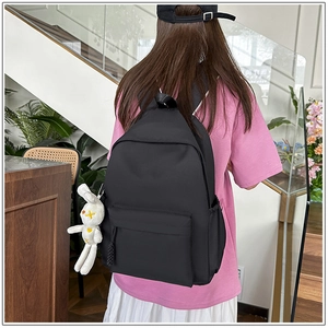 Rear view of a black minimalist backpack with a white rabbit plush charm in a bright room
