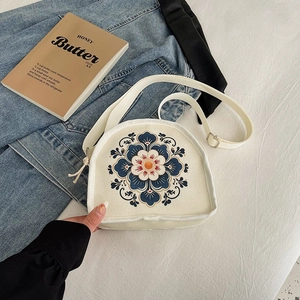 Chic cream canvas crescent bag with blue floral embroidery and adjustable strap