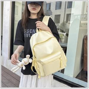 Detail of light yellow backpack with plush bunny charm and textured front zipper pocket