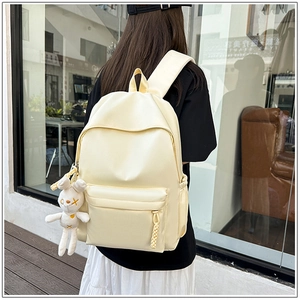 Rear view of cream college backpack with cute plush rabbit charm on city street