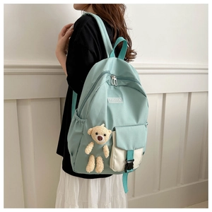 Detail of mint green canvas backpack with plush bear charm worn by a child in daily life