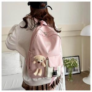Pink toddler backpack featuring cream front pocket and plush bear charm on white sofa