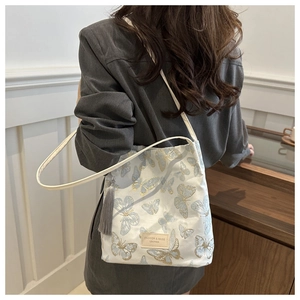 Detail of white canvas tote bag featuring butterfly embroidery and grey tassel accent