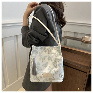 Detail of butterfly embroidery on a beige canvas tote bag with stylish grey tassel accent