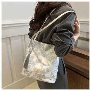 Detail view of butterfly embroidery and tassel charm on a white tote bag