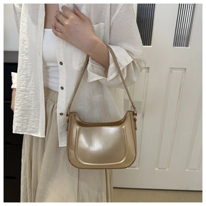 Detail of light gold metallic hobo bag worn on shoulder with minimal white outfit